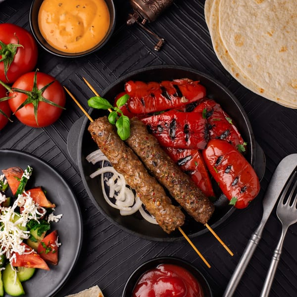 Arzeh Grill's Lebanese kofta skewers with grilled red peppers, fresh salad, and sauces on a black table.
