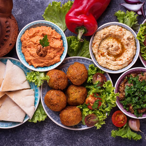 A Lebanese mezze platter with falafel, hummus, muhammara, baba ghanoush, pita bread, and fresh vegetables.